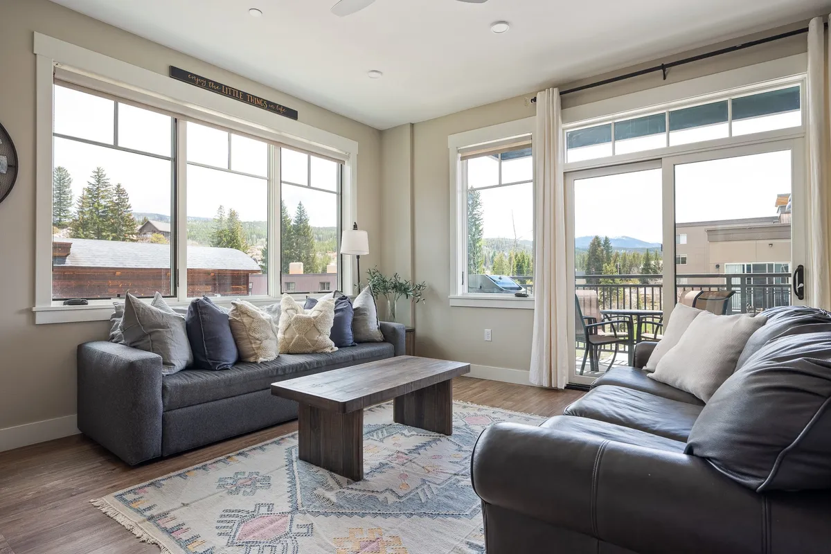 A cozy living area with a sofa adorned with decorative pillows, a coffee table, and large windows that flood the space with light. The inviting setting hints at flexible sleeping arrangements, such as a queen sleeper sofa, and a comfortable atmosphere for families.