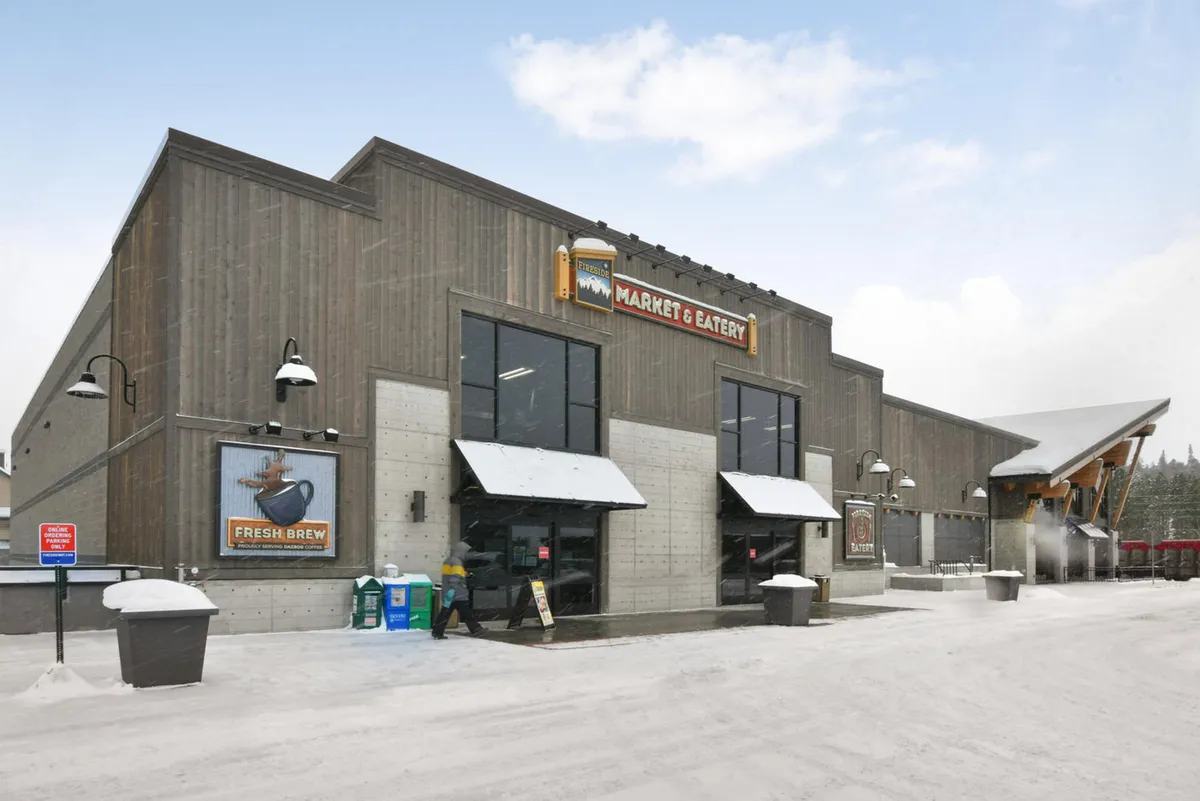 A cozy, snow-covered market and eatery with visible signage near the main entrance, inviting guests to shop for groceries, enjoy a meal, or gather with friends in a welcoming atmosphere.