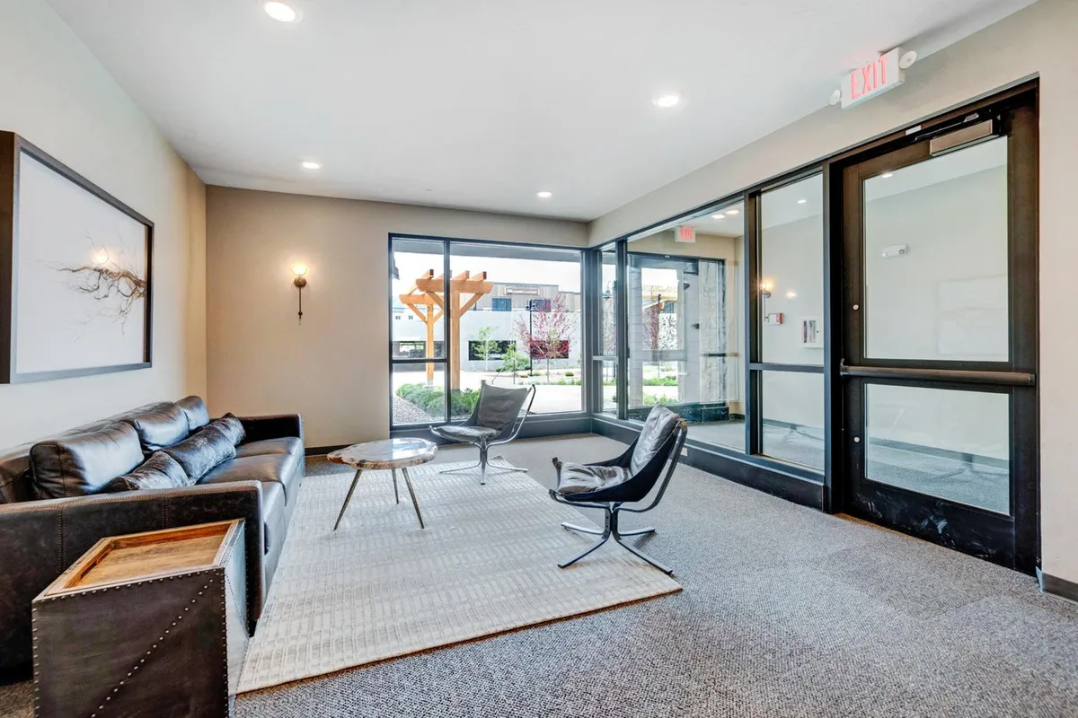 A bright, inviting living area with a sofa, chairs, coffee table, and large windows that let in abundant natural light. The scene showcases a comfortable social setting with a strong sense of openness and connection to the outdoors.